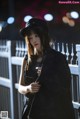 A woman in a black dress and hat standing next to a fence.