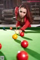 A woman in a red dress is playing pool.