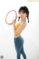 A woman in a yellow top and blue leggings holding a hula hoop.