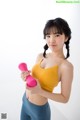 A woman in a yellow top holding a pink dumbbell.