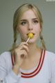 A woman holding a yellow lollipop in her mouth.