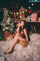 A woman sitting on a pile of snow next to a Christmas tree.