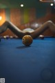 A woman laying on a pool table next to a pool ball.