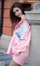 A woman in a pink raincoat leaning against a wall.