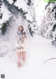 A woman standing in the snow in front of a tree.