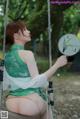 A woman sitting on a swing holding a fan.