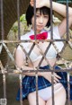 A woman in a school uniform leaning against a fence.