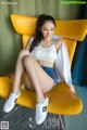 A woman sitting on a yellow chair wearing white sneakers.