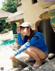 A woman in a blue shirt and a white hat crouching down by a pool.