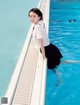 A woman in a school uniform leaning on the edge of a swimming pool.