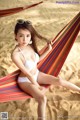 A woman in a white bikini sitting in a hammock on the beach.