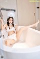 A woman in a white lingerie sitting in a bathtub.