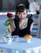 A woman sitting at a table with a cup of coffee and a rose.