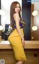 A woman in a yellow skirt leaning against a mirror.