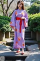 A woman in a purple kimono standing in front of a pond.