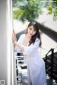 A woman in a white robe leaning against a wall.