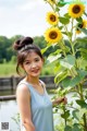 A woman standing next to a tall sunflower in a field.