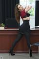 A woman in a red top and black skirt posing in front of a desk.