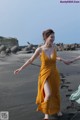 A woman in a yellow dress is walking on the beach.