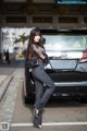 A woman leaning against the back of a black car.